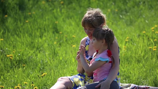 The mother with daughter blowing on a dandelion sitting in the flower meadow
