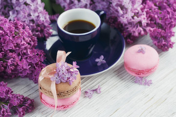 Fototapeta na wymiar Cup of black coffee, lilac flowers and sweet pastel french macar