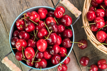 Red cherries in metal bucket and basket on a wooden background.