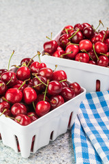 Colanders with red organic cherries on kitchen table.