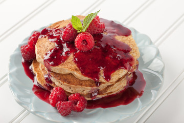 Whole wheat oatmeal pancakes with boysenberry sauce topped with red raspberries and a mint sprig - macro shot