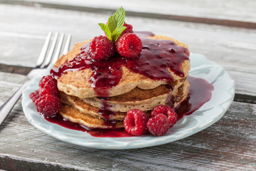 Macro shot of Whole wheat oatmeal pancakes with boysenberry sauce topped with red raspberries and a mint sprig