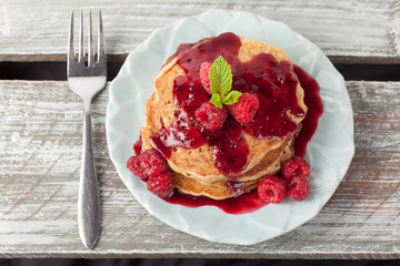 Top view - Whole wheat oatmeal pancakes with boysenberry sauce topped with red raspberries and a mint sprig on a weathered barn wood table
