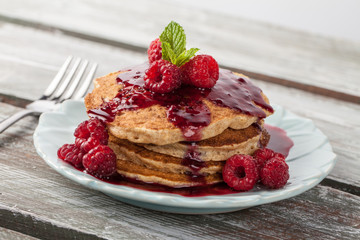 Side view - Whole wheat oatmeal pancakes with boysenberry sauce topped with red raspberries and a mint sprig