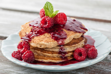 Whole wheat oatmeal pancakes with boysenberry sauce topped with red raspberries and a mint sprig macro shot on a weathered barn wood table