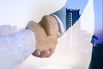 Double exposure closeup of businessmans handshake on city background.