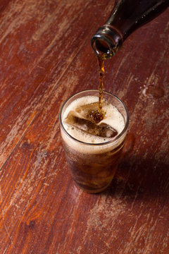 Pouring cola into the glass on wooden table