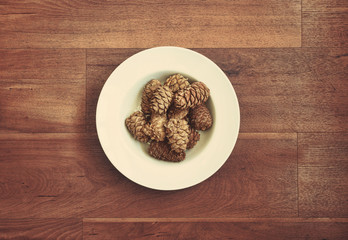 Cedar cones in big white plate on wooden background. Natural interior design elements, healthy food