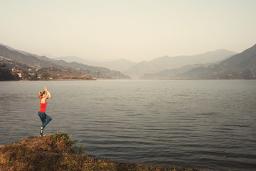 Young girl doing yoga exercise in beautiful mountain lake landscape. Summer, sport outdoor, relaxation