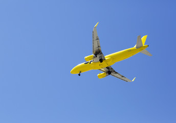 The plane is flying against the blue sky. The bright yellow airplane flies on a summer day high in the sky.