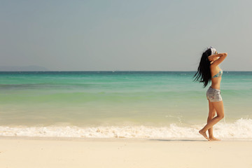 Fototapeta na wymiar Girl in swimsuit walking on sea beach, relaxing and sunbathing. White sand, beautiful coast landscape