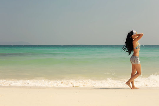 Girl in swimsuit walking on sea beach, relaxing and sunbathing. White sand, beautiful coast landscape