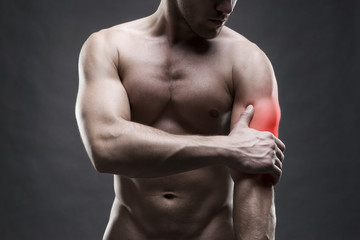 Obraz premium Pain in the elbow. Muscular male body. Handsome bodybuilder posing on gray background