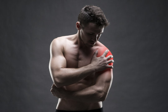 Pain in the shoulder. Muscular male body. Handsome bodybuilder posing on gray background