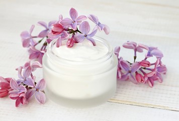 Jar of white facial cream, fresh flowers. Sweet floral aroma skincare.