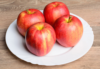 Naklejka na ściany i meble Red apples on white plate and wood table