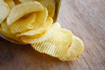 Opened pack with potato chips over wooden table
