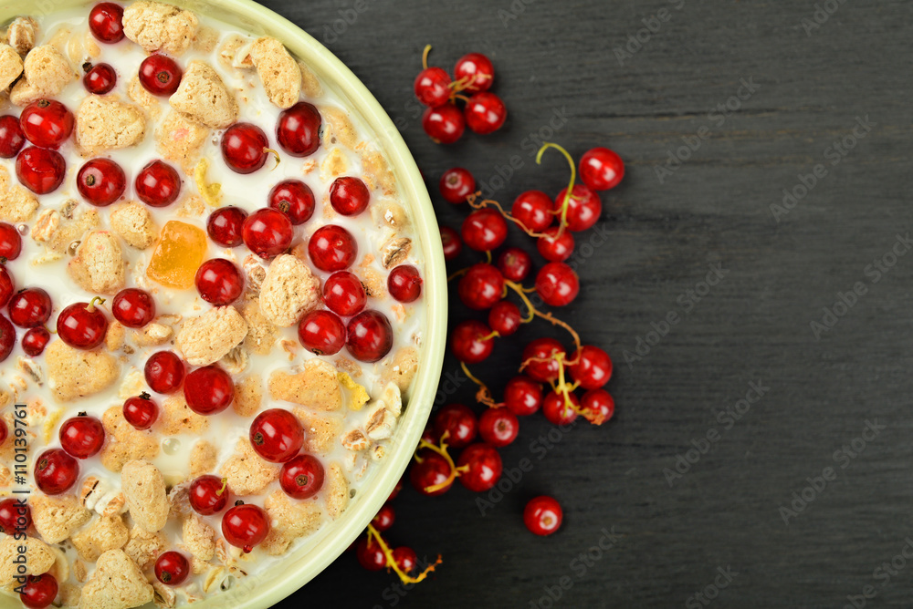 Poster milk in a bowl with granola and red berries scattered on a dark wooden background