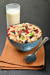full bowl of muesli with berries and spoon on a napkin near to the glass of milk on a dark wooden background