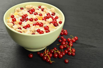 milk in a bowl with granola and red berries scattered on a dark wooden background