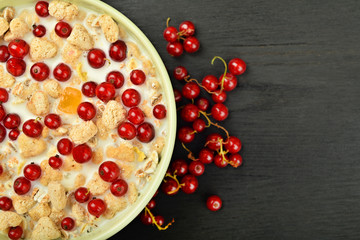 milk in a bowl with granola and red berries scattered on a dark wooden background