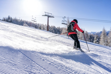 Fototapeta na wymiar Female skiier dressed in red jacket enjoys slopes in Italy with sun behind her.