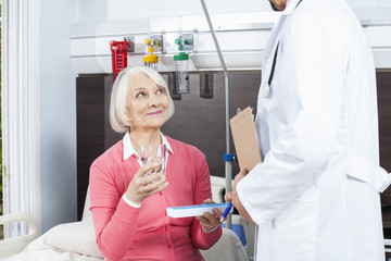 Patient Holding Water Glass And Medicine While Looking At Doctor