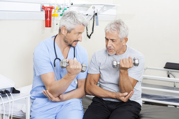 Physiotherapist Assisting Senior Man In Lifting Dumbbells