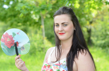 Beautiful young woman holdin a fan in the park