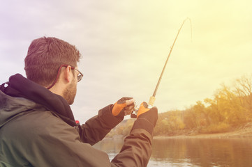 Young man fishing on a river from the boat at sunset