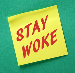 The words Stay Woke in red text on a yellow sticky note as a reminder to remain aware and stay informed about politics and other issues