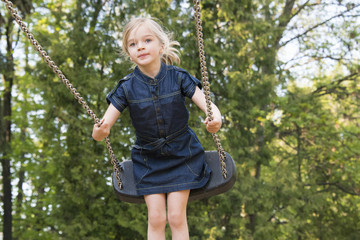 Little child blond girl having fun on a swing outdoor. Summer playground. Girl swinging high 