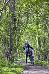 Obraz premium young blond girl with bicycle amongst fresh green spring foliage