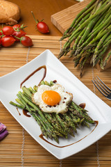Asparagi verdi con uovo al tegamino su un piatto in ceramica bianco  ambientato