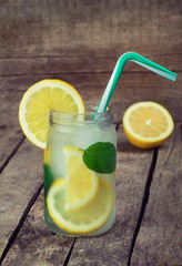 homemade lemonade with lemon, mint and straw in jar on a wooden