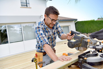 Carpenter cutting planks for wooden deck - obrazy, fototapety, plakaty