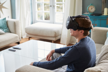 Obraz premium Man Sitting On Sofa At Home Wearing Virtual Reality Headset