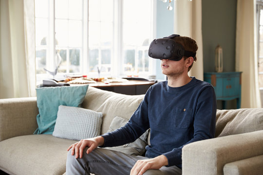 Man Sitting On Sofa At Home Wearing Virtual Reality Headset