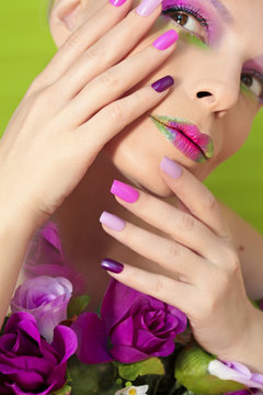 Разноцветные сиреневые ногти и губы на девушке с розами и зелёным фоном.