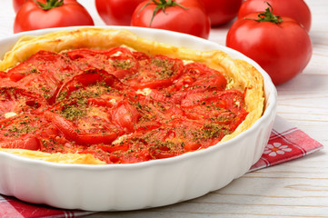 Quiche with creme cheese and tomatoes on white wooden table.