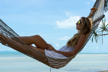 
Young beautiful woman lying in a hammock with laptop in a tropical