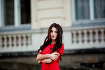 Street fashion concept: Portrait of a beautiful young woman wearing a red dress walking in the city. Old architecture background