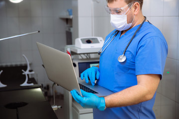 Naklejka premium adult doctor in mask with laptop and medical tools in operating room at the hospital