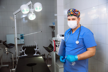 portrait of a doctor in mask with laptop and medical tools in operating room at the hospital. Dressed in professional uniform