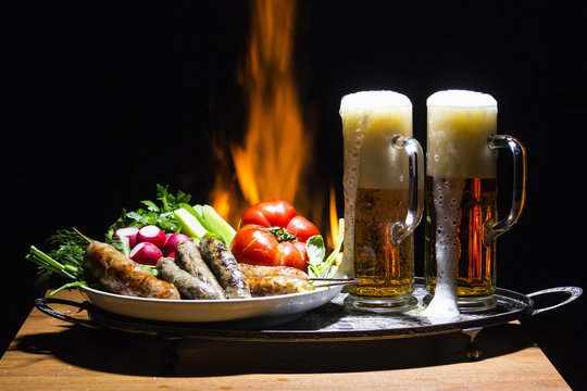 two beers and sausages with flame on background