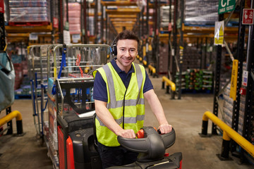 Man on tow tractor at distribution warehouse looks to camera