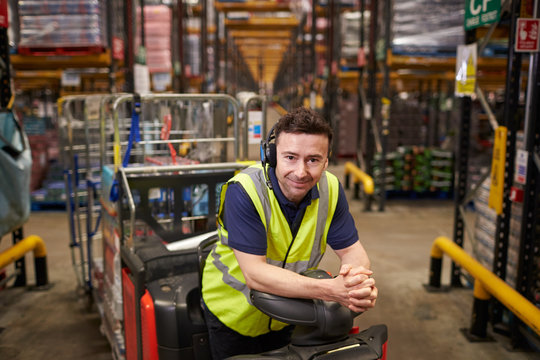 Man on tow tractor in distribution warehouse leans to camera