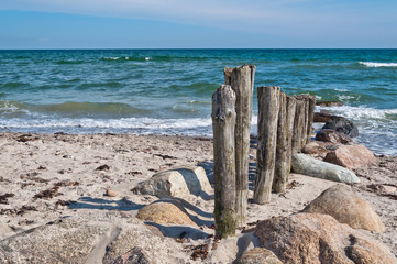Holzpfähle führen vom Strand ins Meer, Textfreiraum links