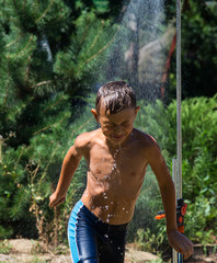Boy under a shower on the garden in hot day