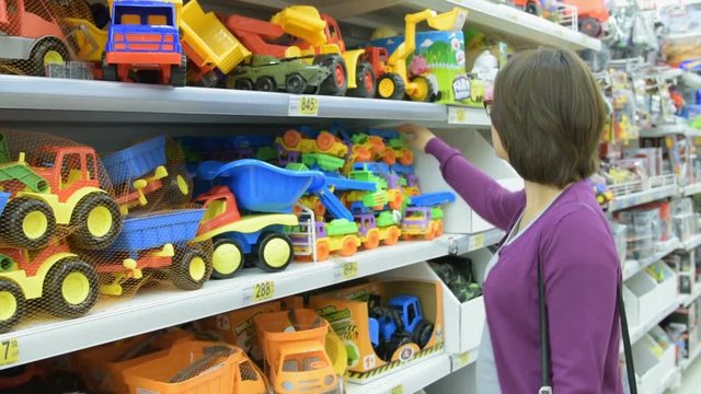 Young woman choosing toy plastic car in the supermarket